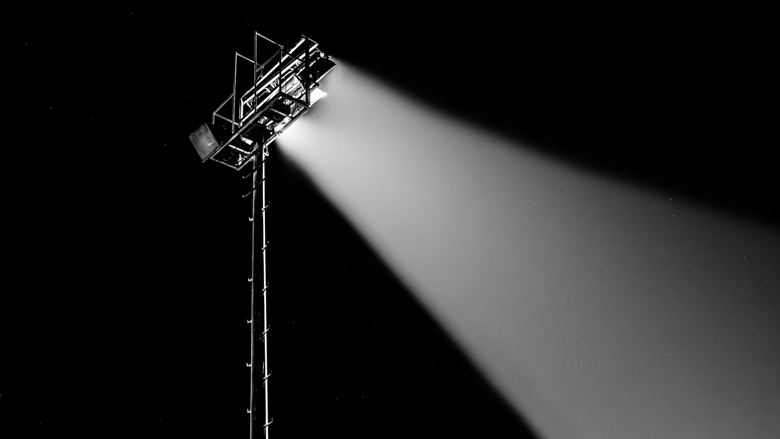 Dramatic spotlight beam shining into the night sky captured in black and white.