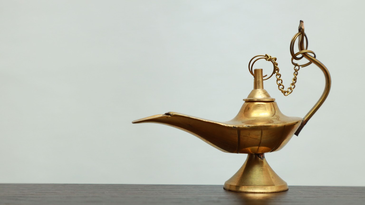 A classic brass oil lamp with a chain, reminiscent of Aladdin's lamp, on a wooden surface.