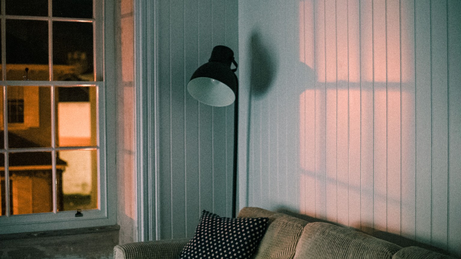 A warm and inviting living room featuring a soft couch and floor lamp casting shadows on the wall.