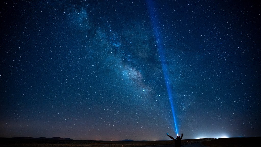 A person stands on a road under the Milky Way, pointing a beam of light into the starry night sky in Karaman, Türkiye.