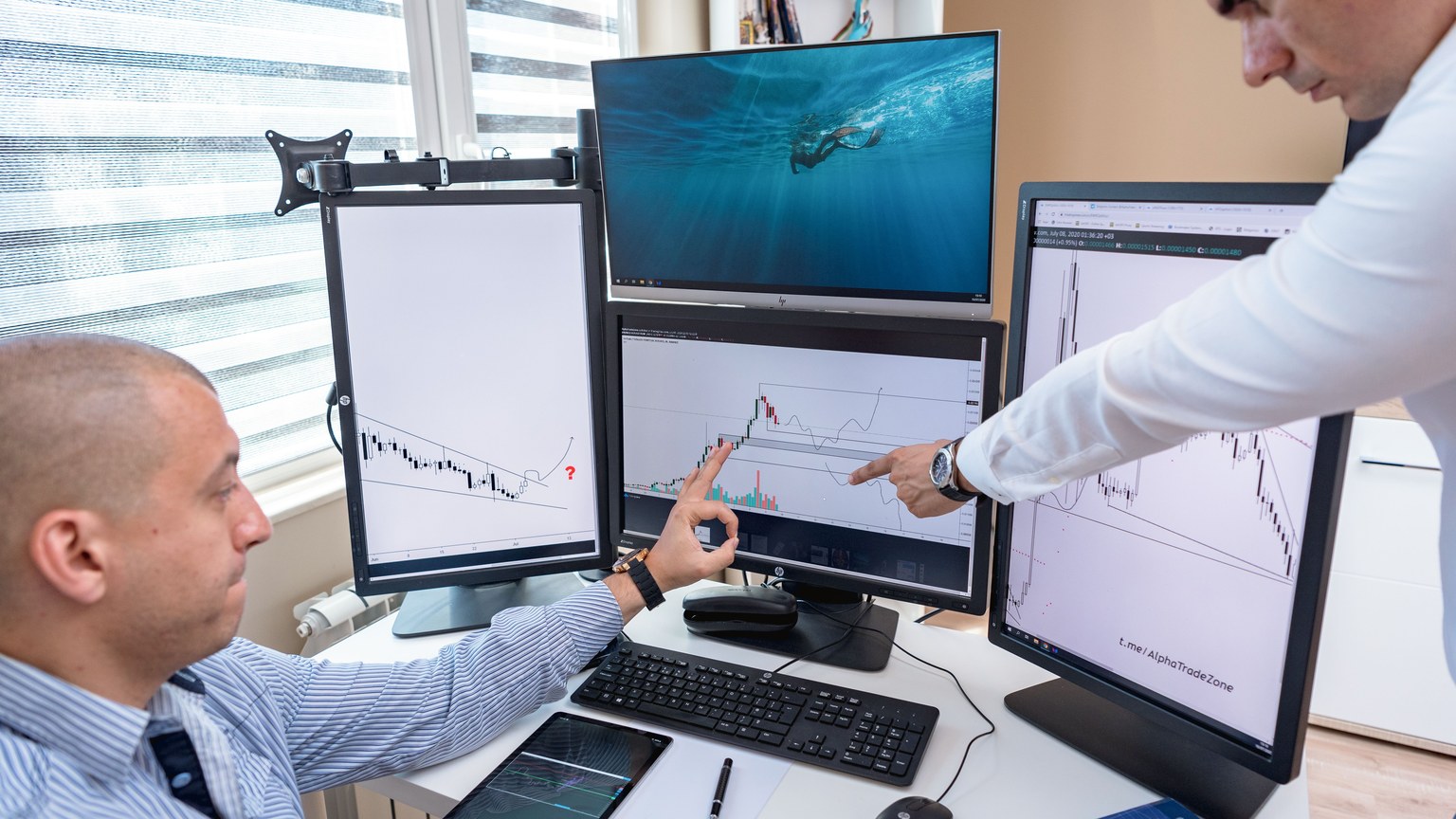 Two business professionals analyzing financial data on multiple computer screens in an office setting.
