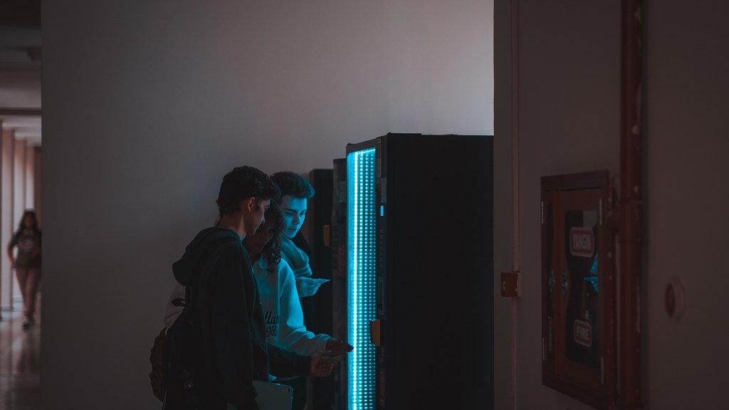 Group of teenagers using a vending machine in a school corridor, captured in ambient lighting.