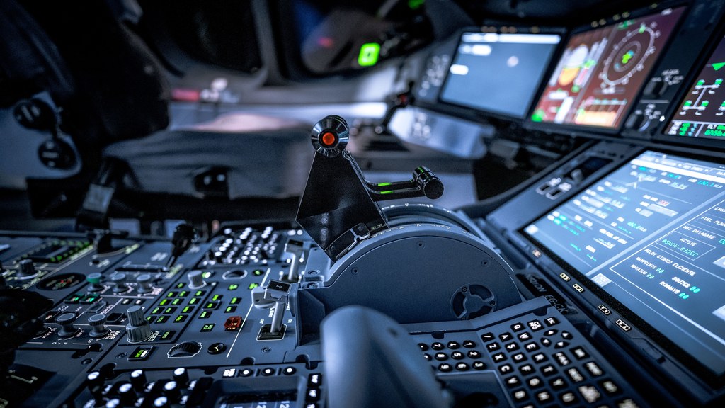 Close-up view of a modern aircraft cockpit with glowing control panels and screens.