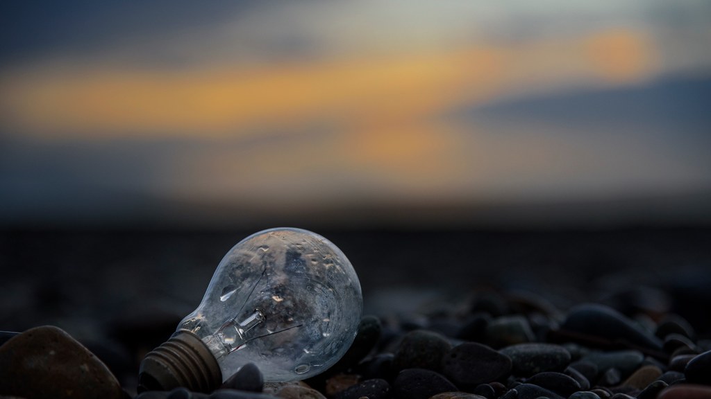 A moody beach sunset with a discarded lightbulb resting on pebbles, symbolizing lost ideas.