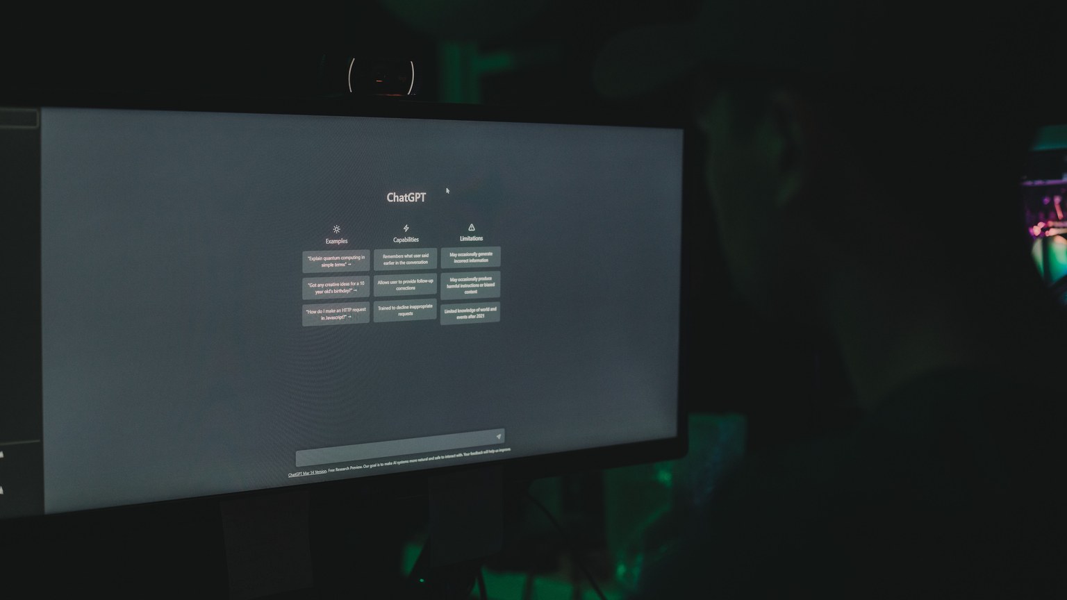 A person interacting with ChatGPT interface on a computer screen in a dimly lit room.