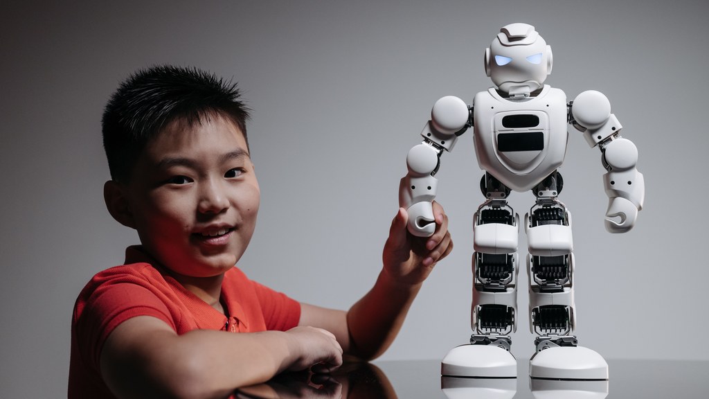A young boy in a red shirt engaging with a humanoid robot indoors.