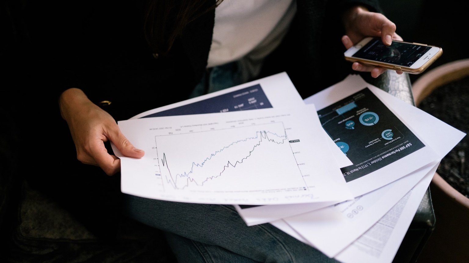 A person reviews stock market graphs on paper and smartphone for business insights.