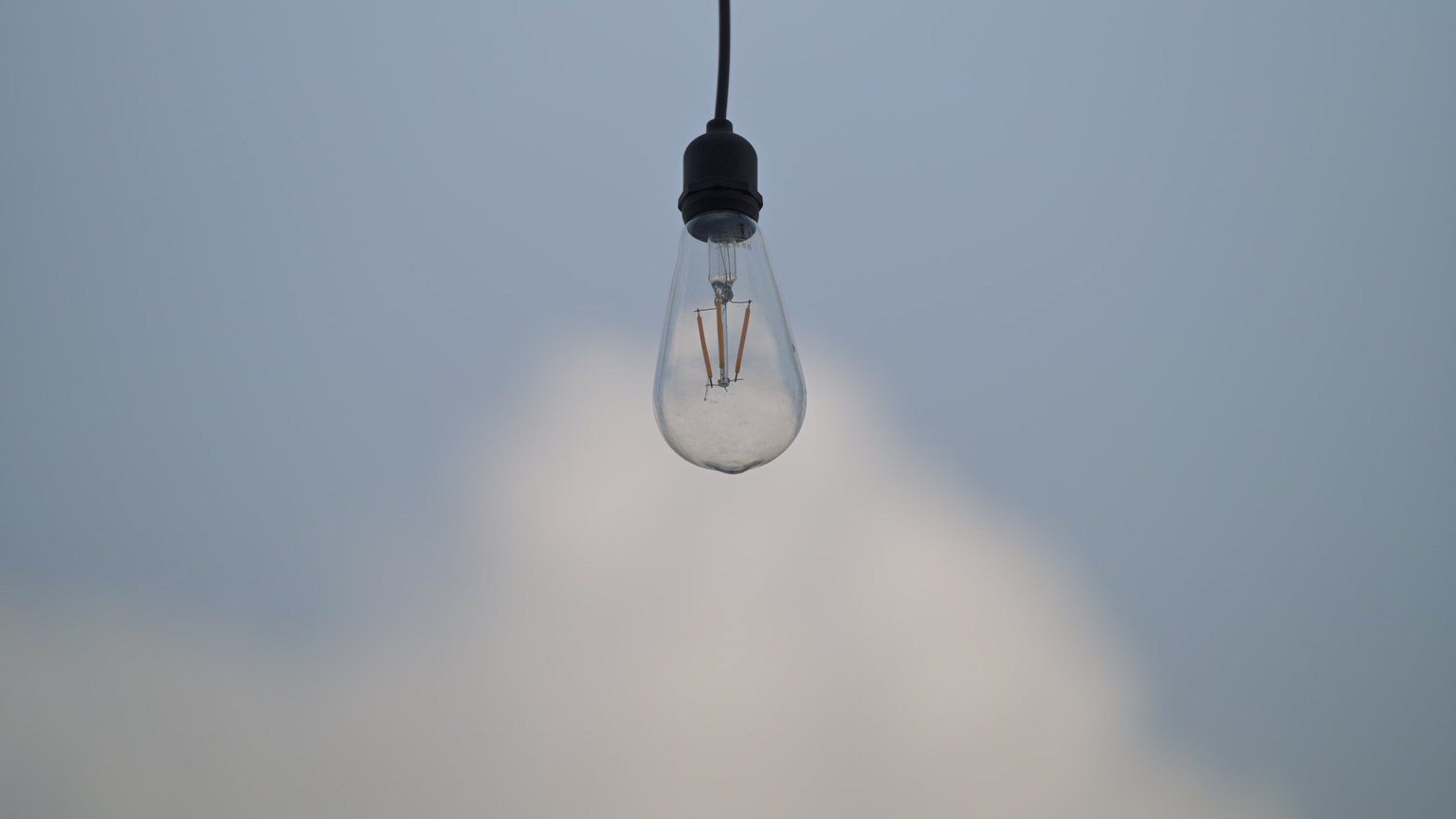 A single light bulb suspended against a soft blue sky, evoking simplicity and innovation.