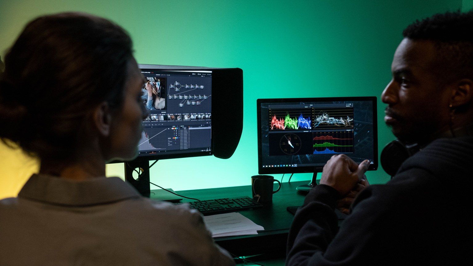 Two colleagues collaborating on video editing, analyzing color grading on dual monitors in a studio.