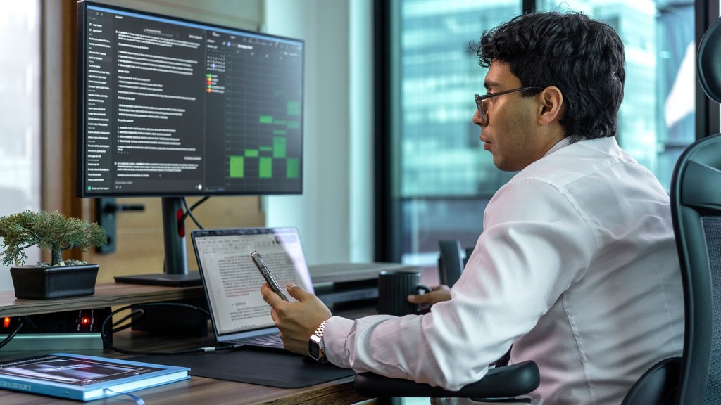 Businessman focused on data analysis on a dual monitor setup in a modern office setting.