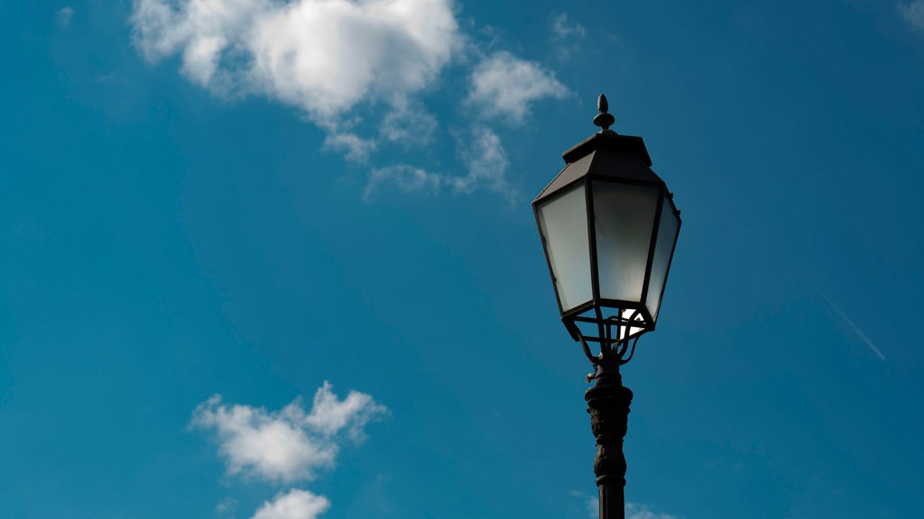 A classic street lamp silhouetted against a bright blue sky with fluffy clouds.
