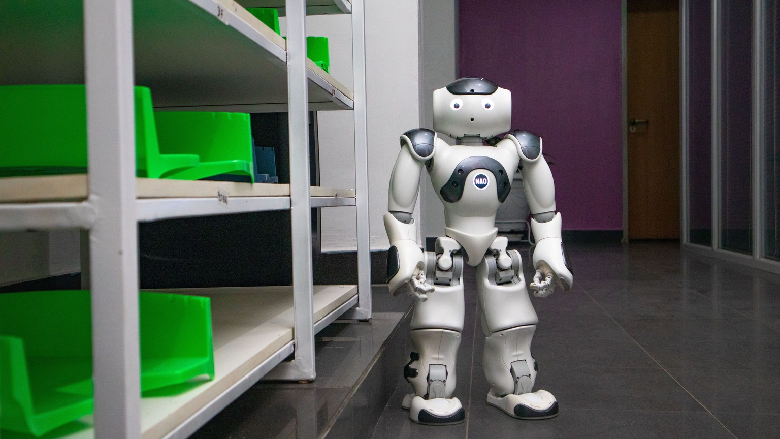 A humanoid robot standing in a modern corridor with shelves, representing futuristic technology.