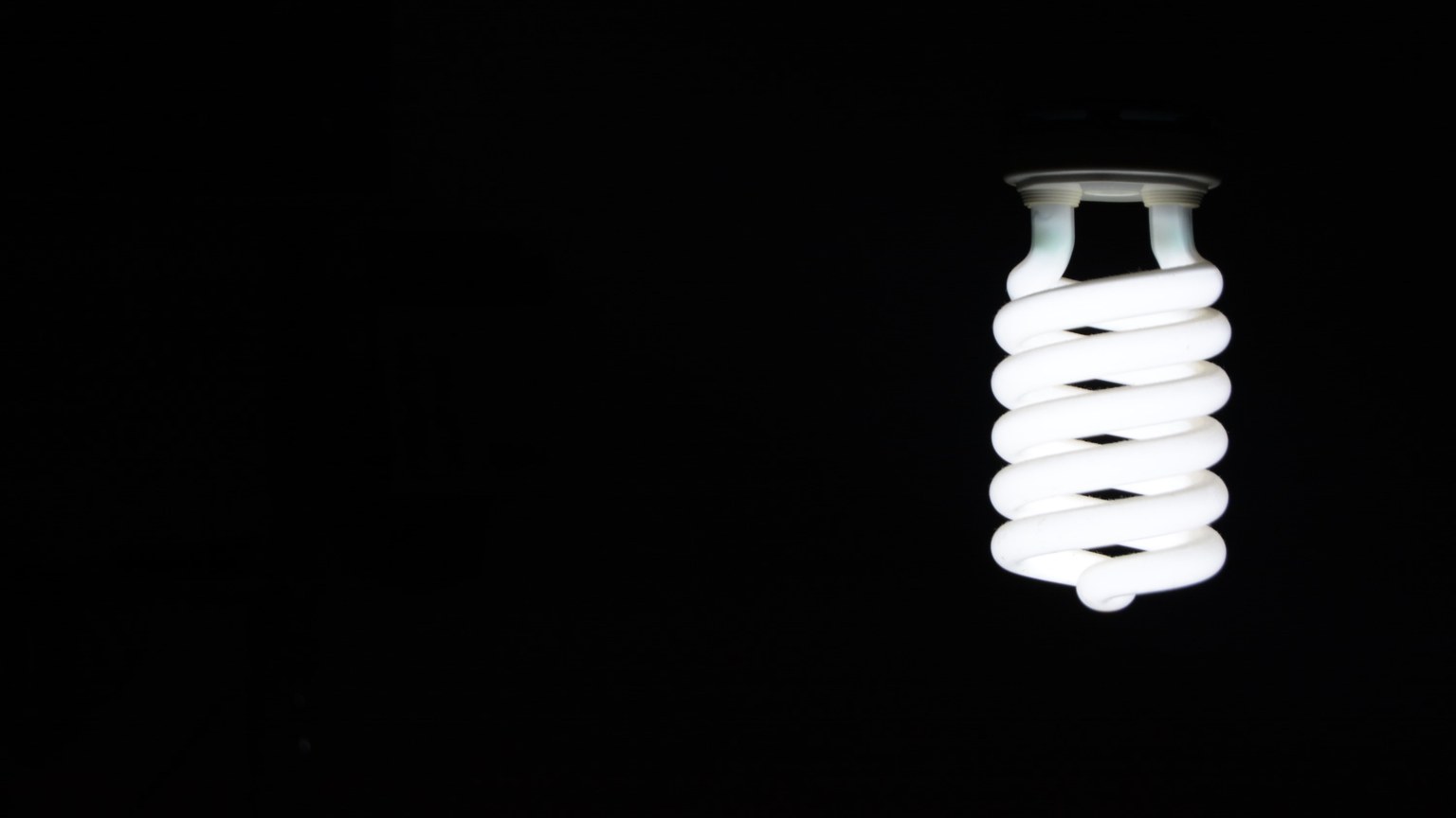 Bright spiral LED lightbulb against black background, artistic minimalism.