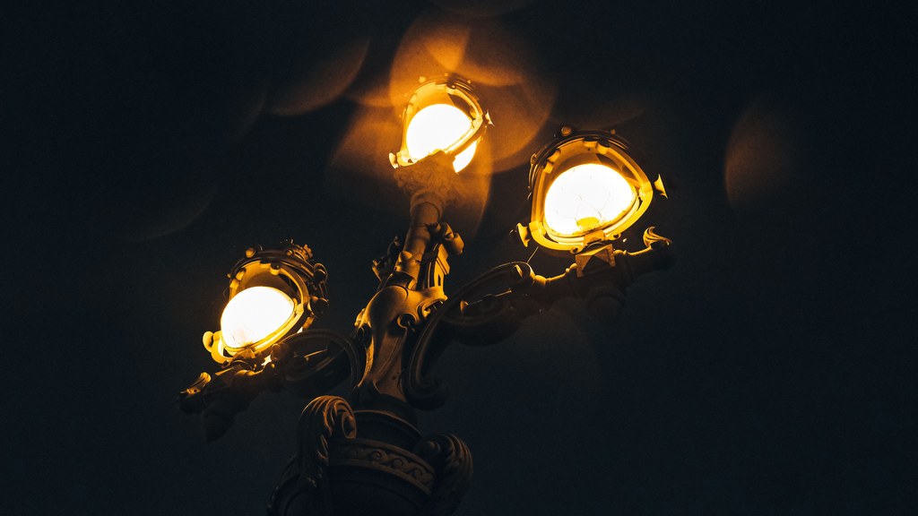 A close-up of a vintage street lamp illuminating the night sky with warm glowing lights.