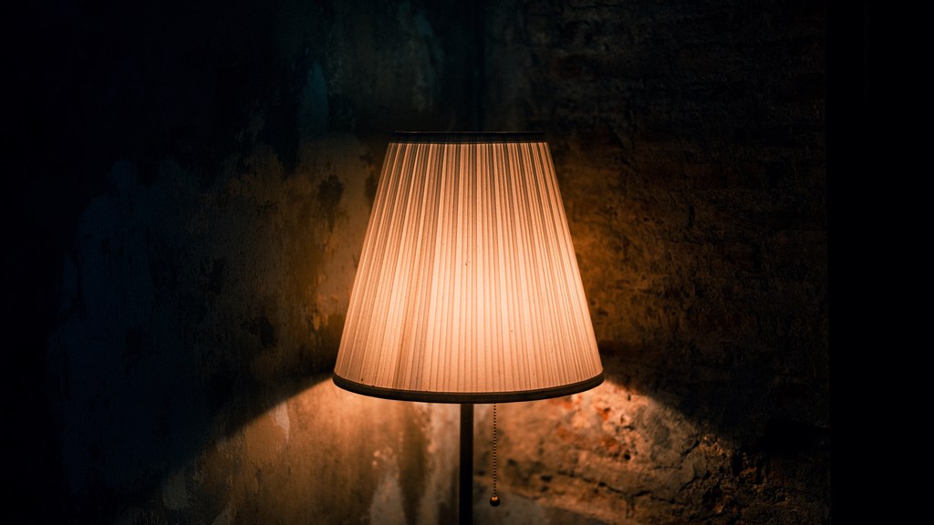 Warmly lit lamp casting shadows on a textured wall in a dark, moody setting.