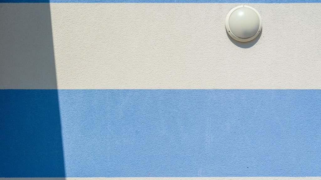 Close-up of a blue and white striped wall with a round wall lamp casting a shadow.