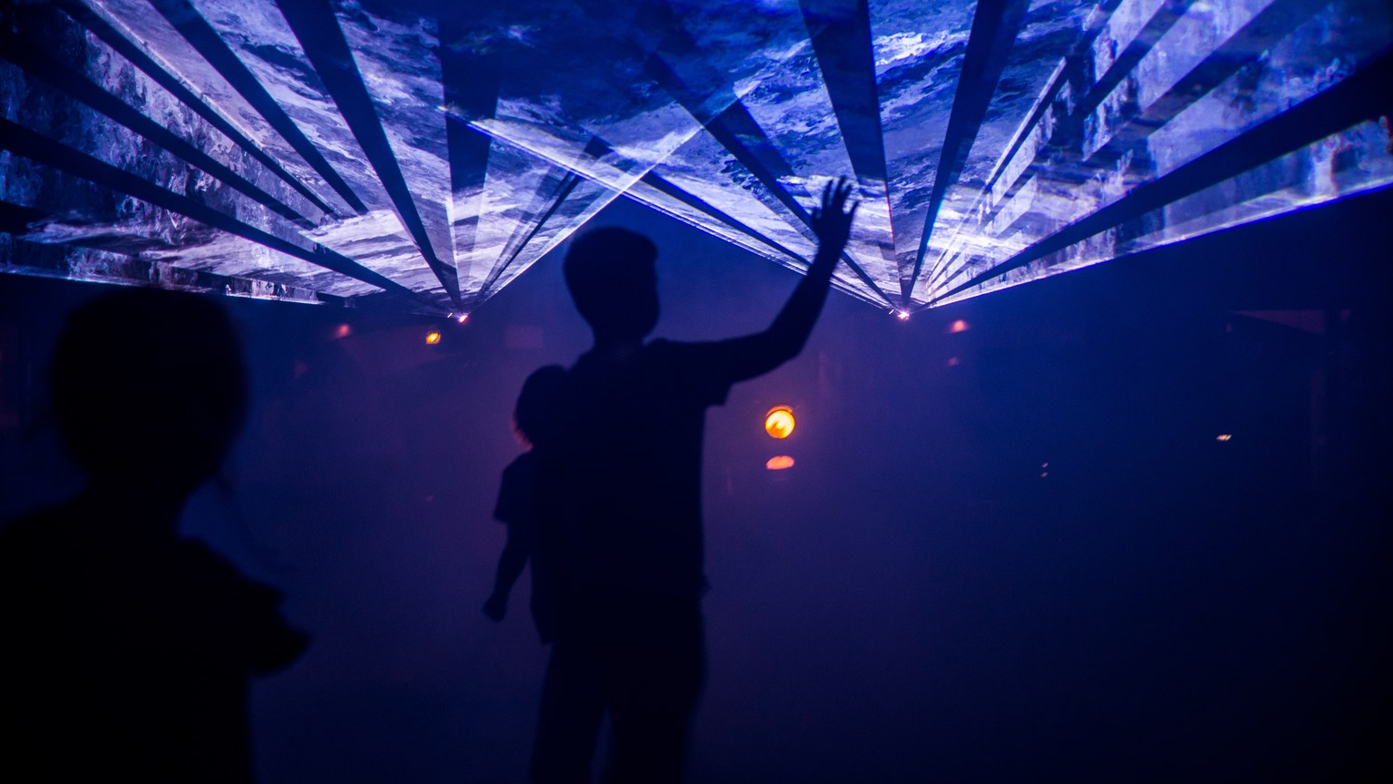 Silhouette of people interacting with an artistic indoor light display, creating a mesmerizing visual effect.