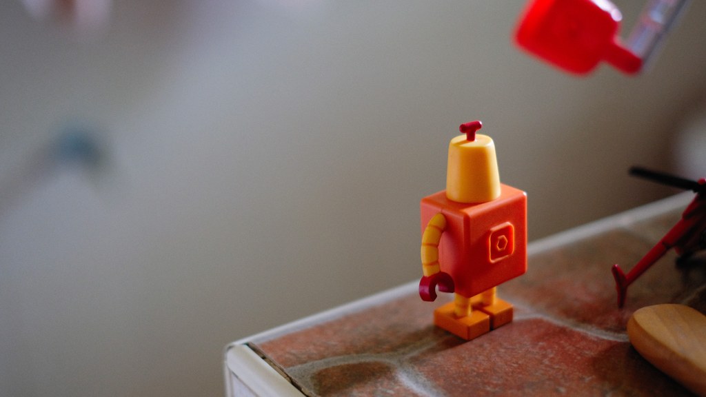 Close-up of a small colorful robot toy standing on a brown surface indoors.