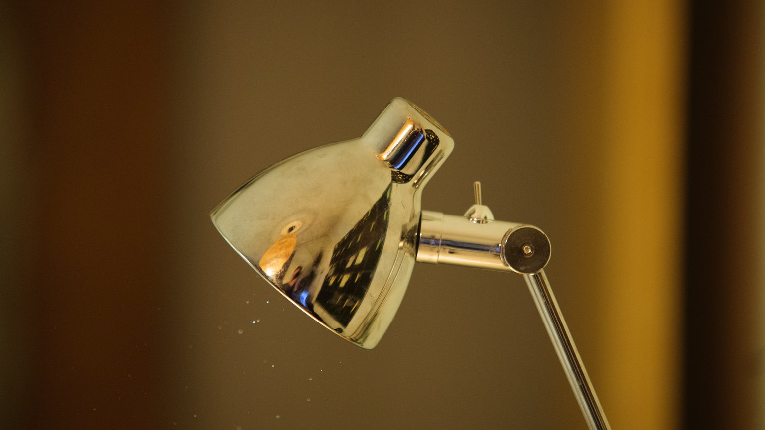 A close-up image of a sleek metallic desk lamp featuring a reflection in indoor lighting.