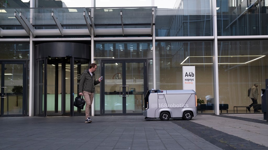 A man encounters a delivery robot outside a modern glass building.