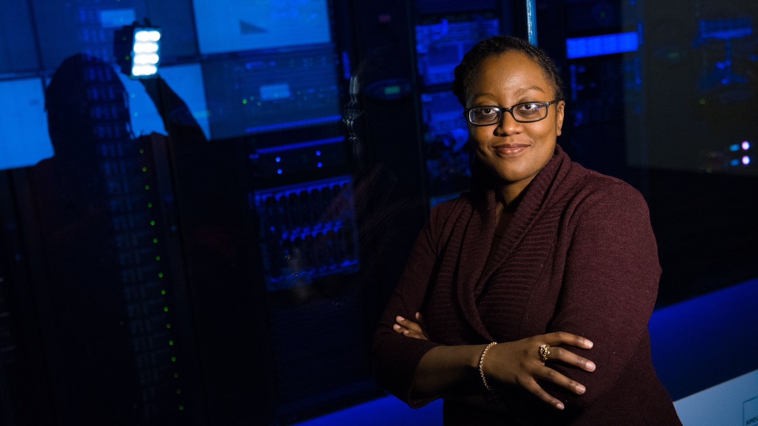 Professional woman standing confidently in a data center, surrounded by glowing servers.