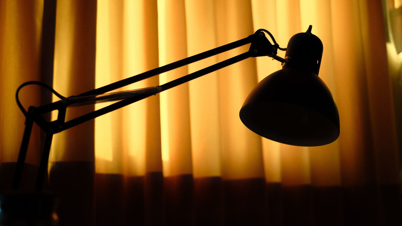 Dramatic silhouette of a desk lamp with warm backlighting from yellow curtains.