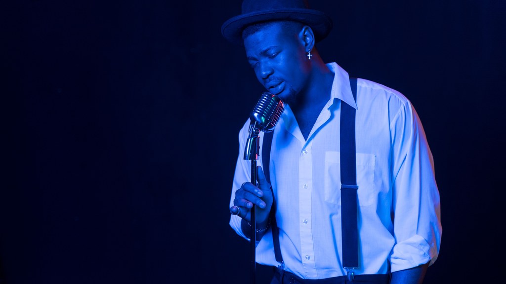 A male vocalist passionately sings under blue stage lighting, exuding emotion and style.