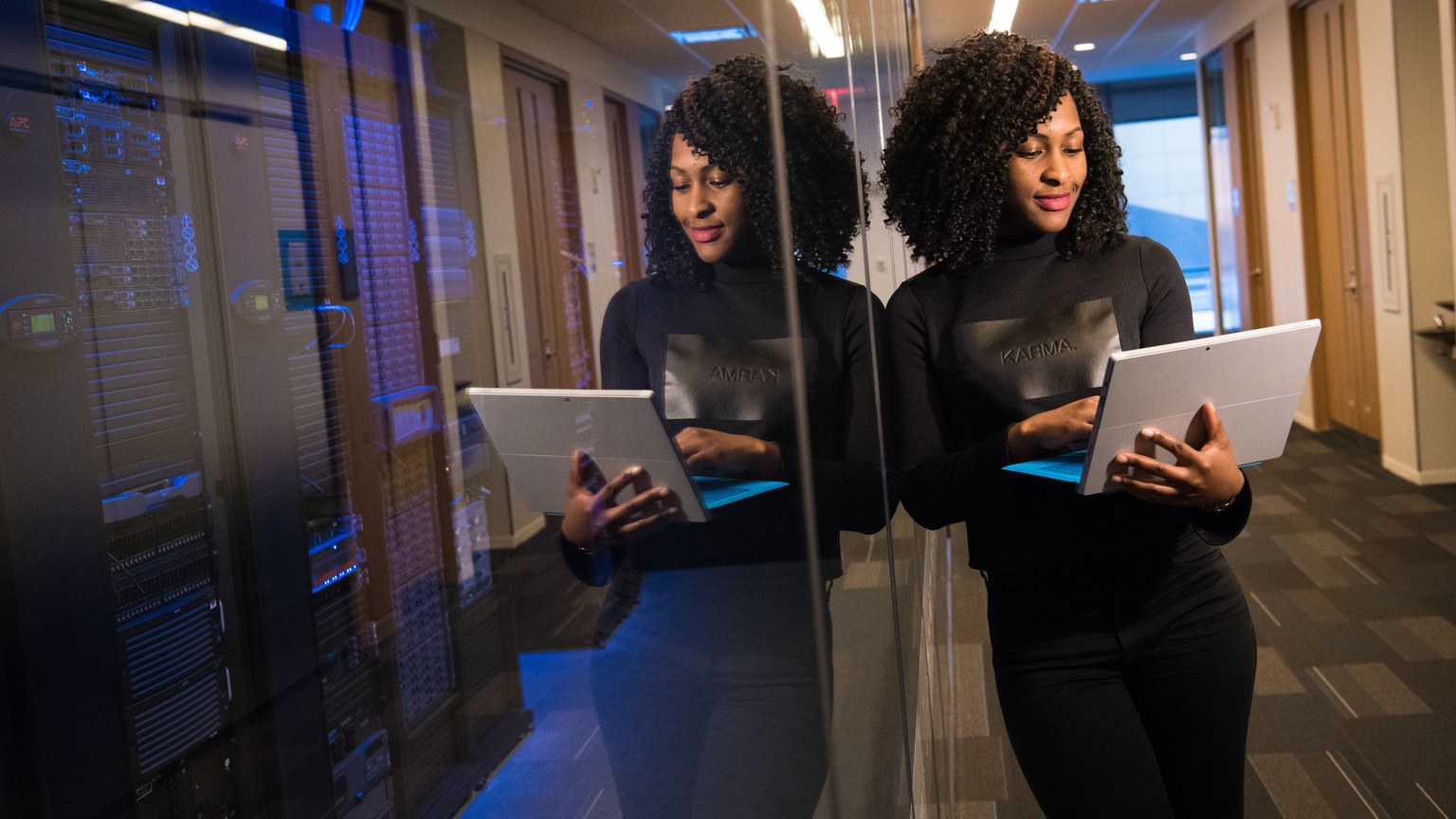 African American woman standing in modern office using laptop, reflecting professionalism and technology engagement.