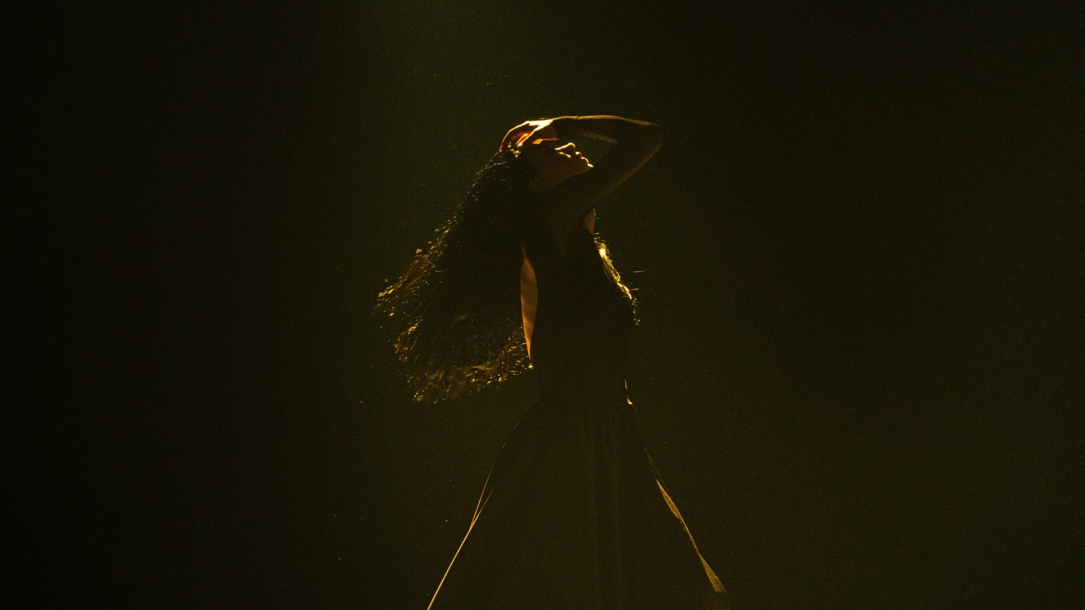 A graceful woman's silhouette dancing under spotlight on a dark stage, capturing movement and emotion.