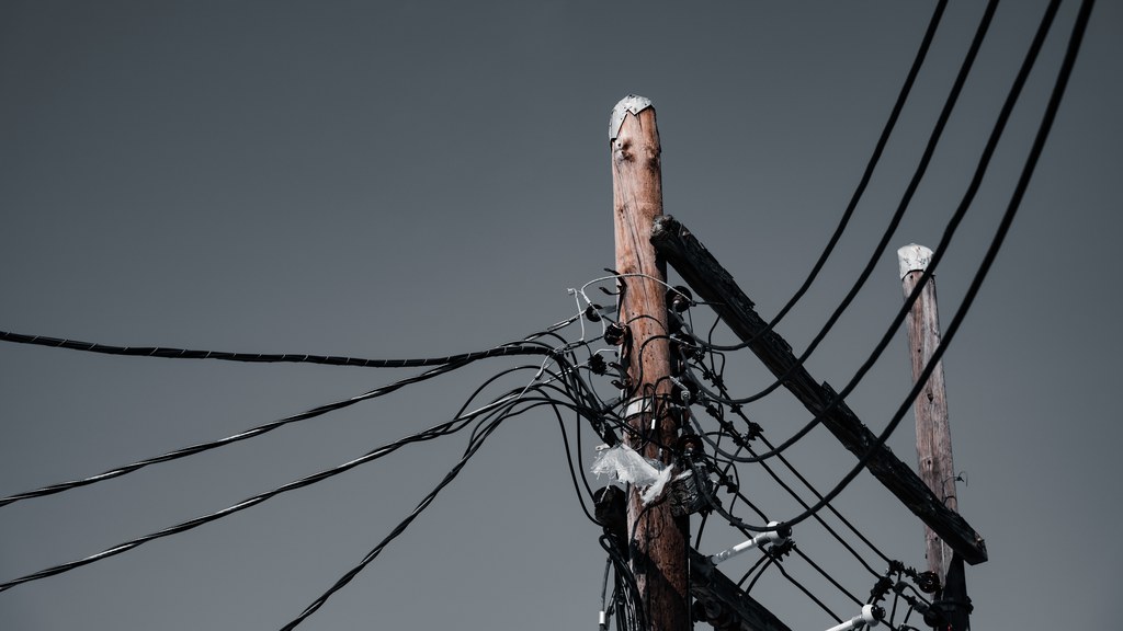 Low angle shot of wooden utility poles with power lines against a gray sky in Orlando, FL.