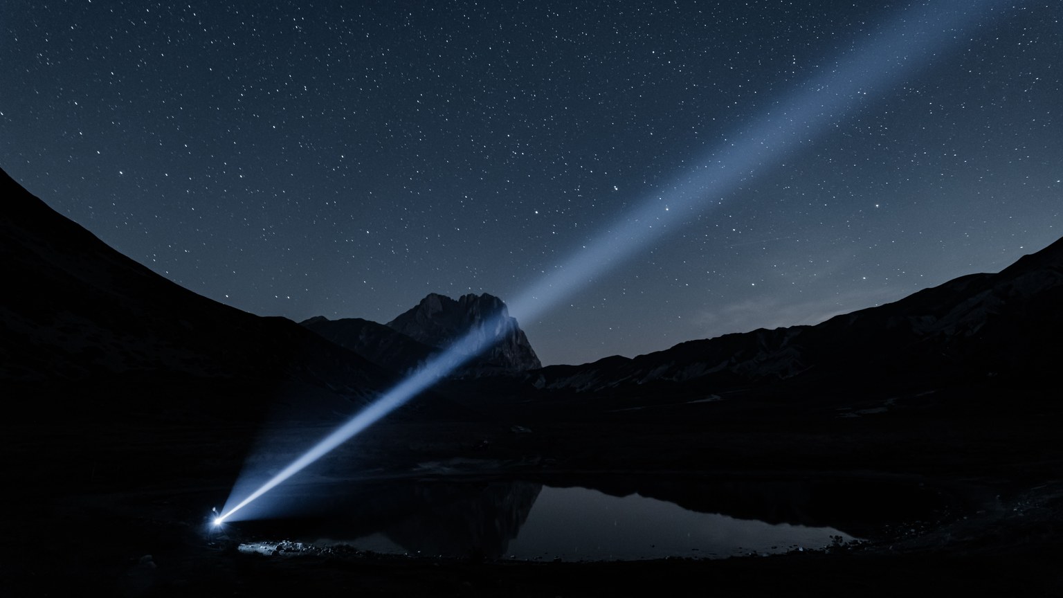 Dramatic night sky with starry landscape and beam of light in the mountains.