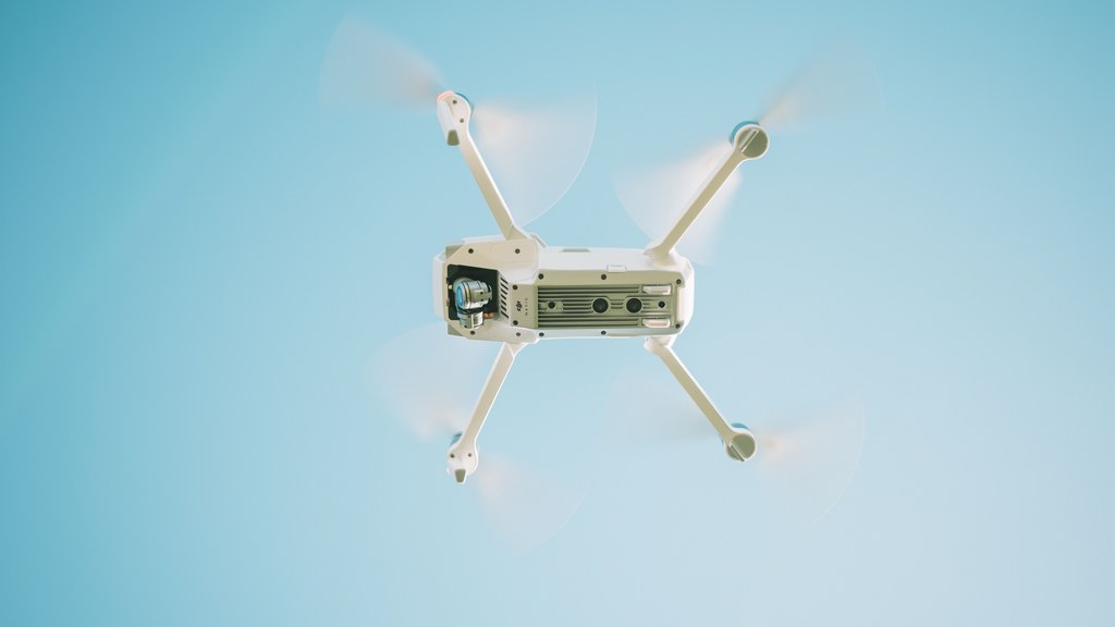 A sleek white drone flying under a clear blue sky, capturing aerial views.