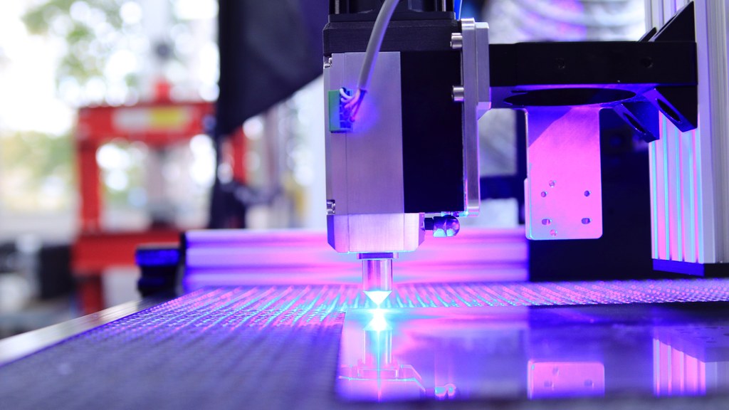 Close-up of a laser engraving machine working indoors with blue light reflection.
