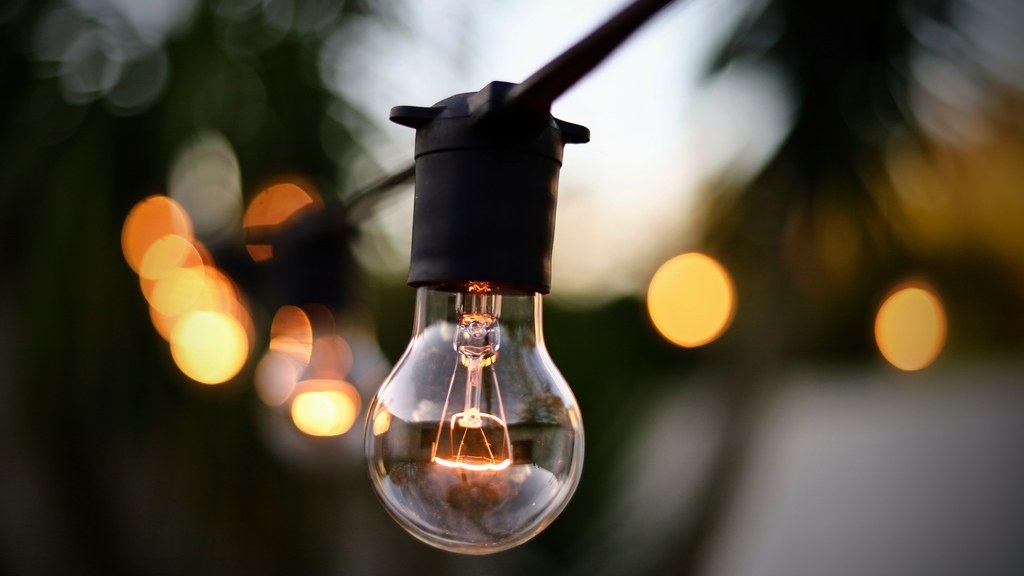 Illuminated light bulb hanging on string with bokeh backdrop outdoors.