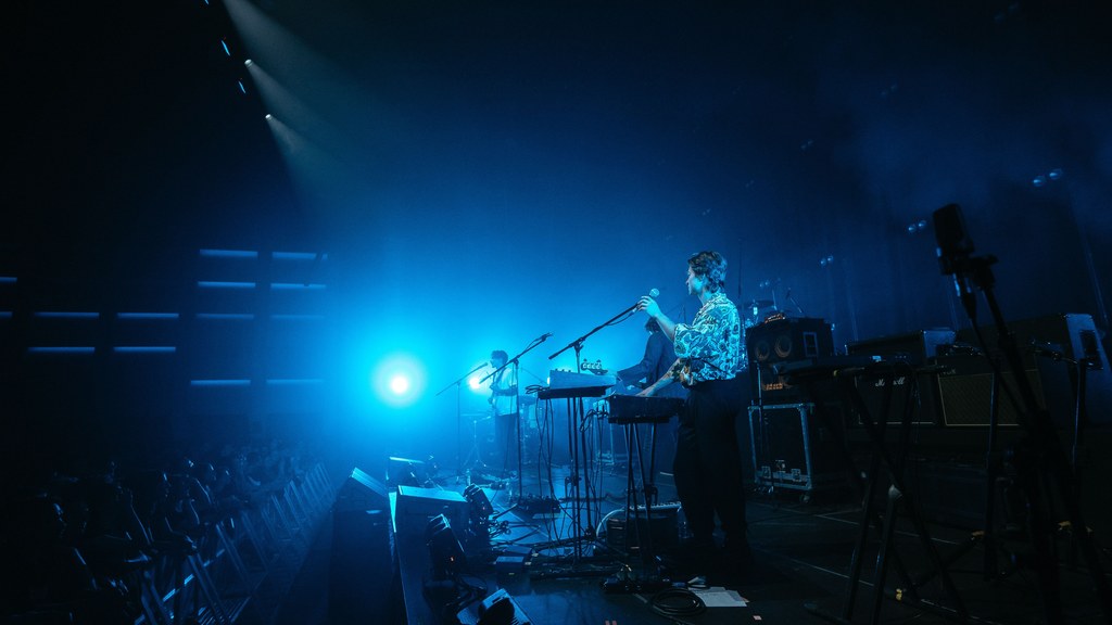 Energetic live band performance on stage with vibrant blue lighting and audience engagement.