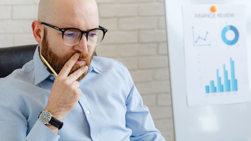 Business analyst in a blue shirt analyzing financial charts on a whiteboard.