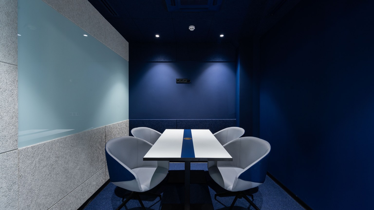 Comfortable chairs placed on carpet at long white desk in modern conference room with blue walls in contemporary business center
