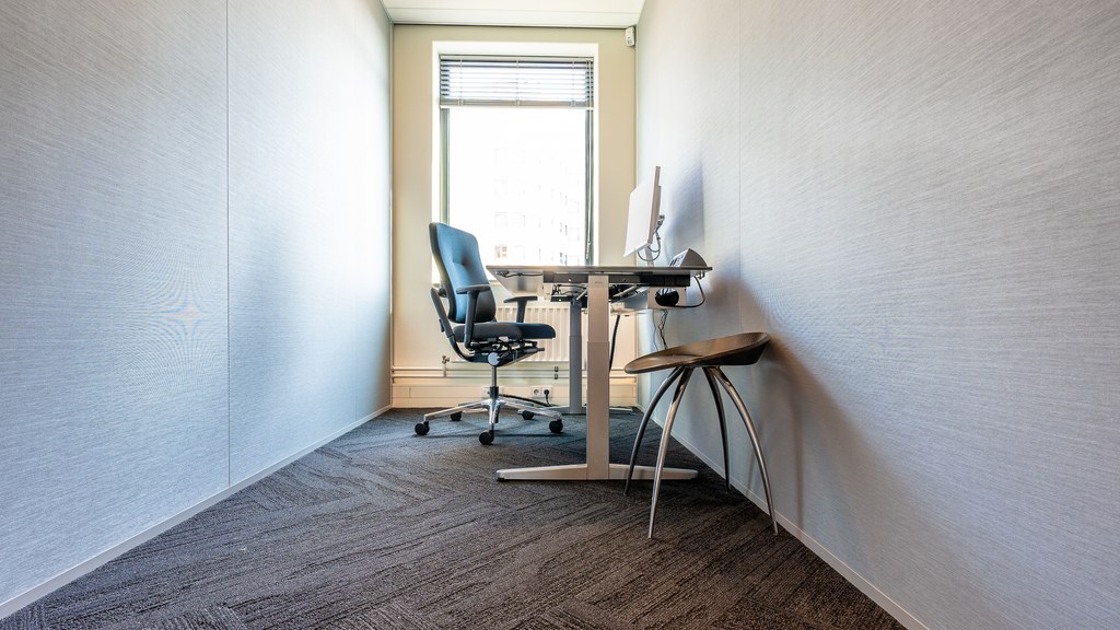 A clean, minimalist office space featuring a desk, chair, and computer by a large window.