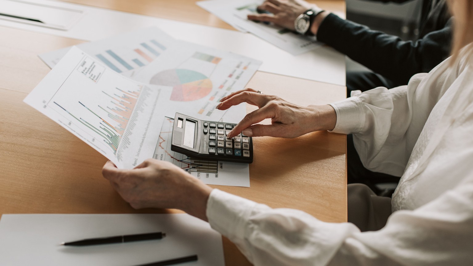 Hands performing financial calculations with charts and a calculator at a meeting table.