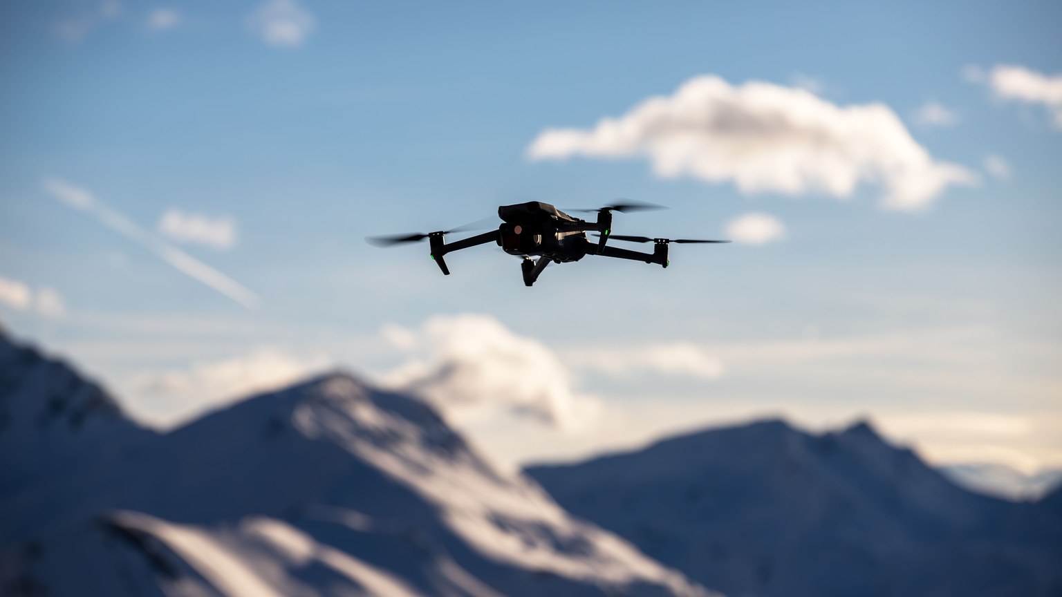 A drone flies over scenic snow-covered peaks under a clear blue sky, capturing breathtaking landscapes.