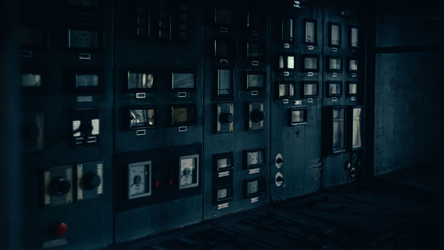 A dark, retro industrial control panel with dials and gauges in a maintenance room.