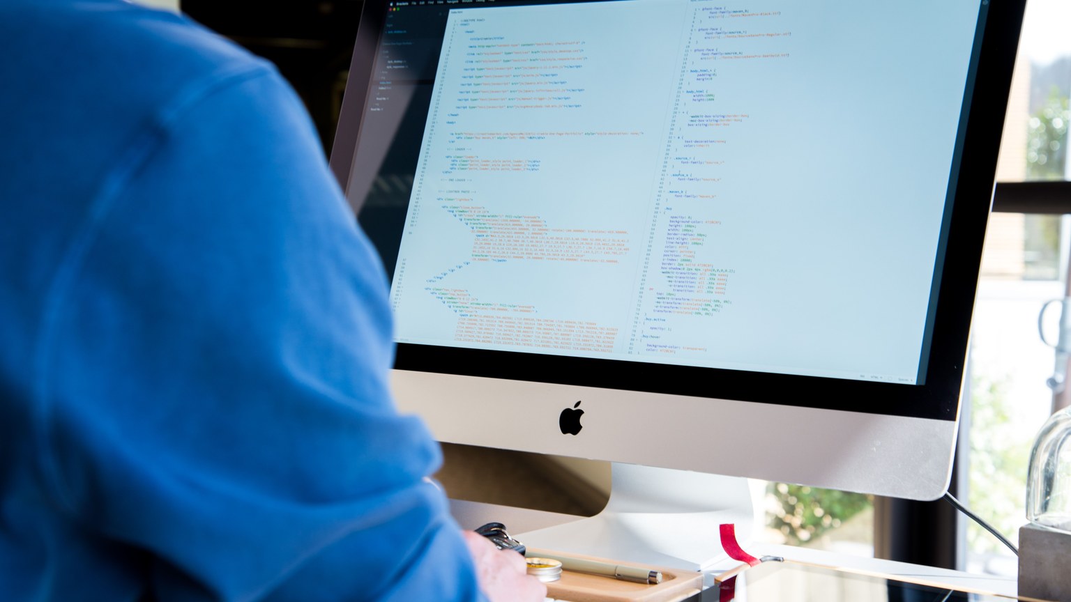 A programmer in a blue shirt coding on an iMac. Perfect for technology or work-related themes.