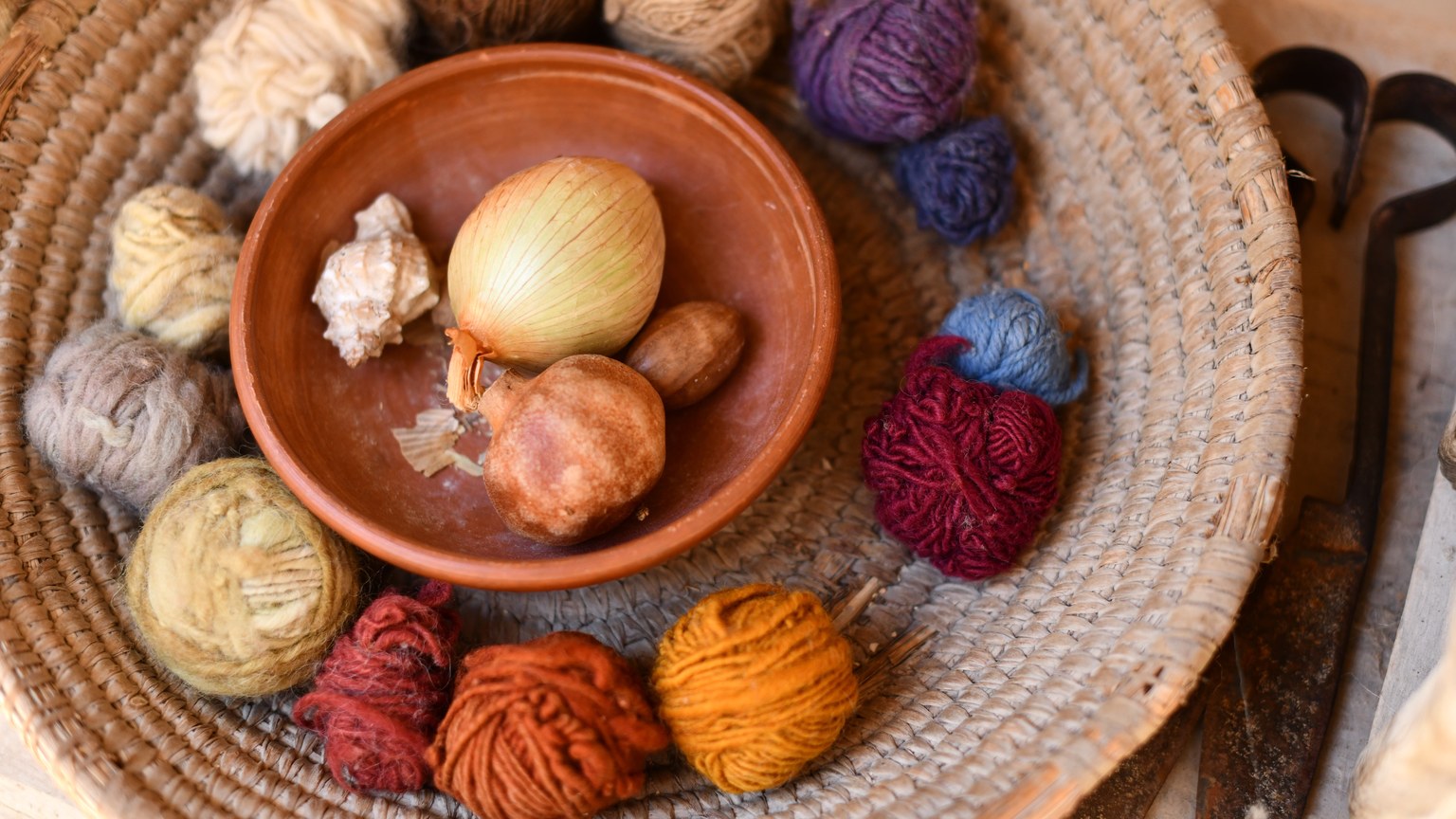 Close-up of colorful yarn balls with onion dye in a rustic basket, highlighting natural dyeing techniques.