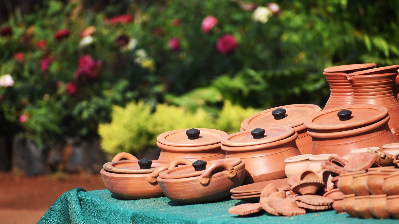 Collection of handmade terracotta pots and plates on display with garden background.