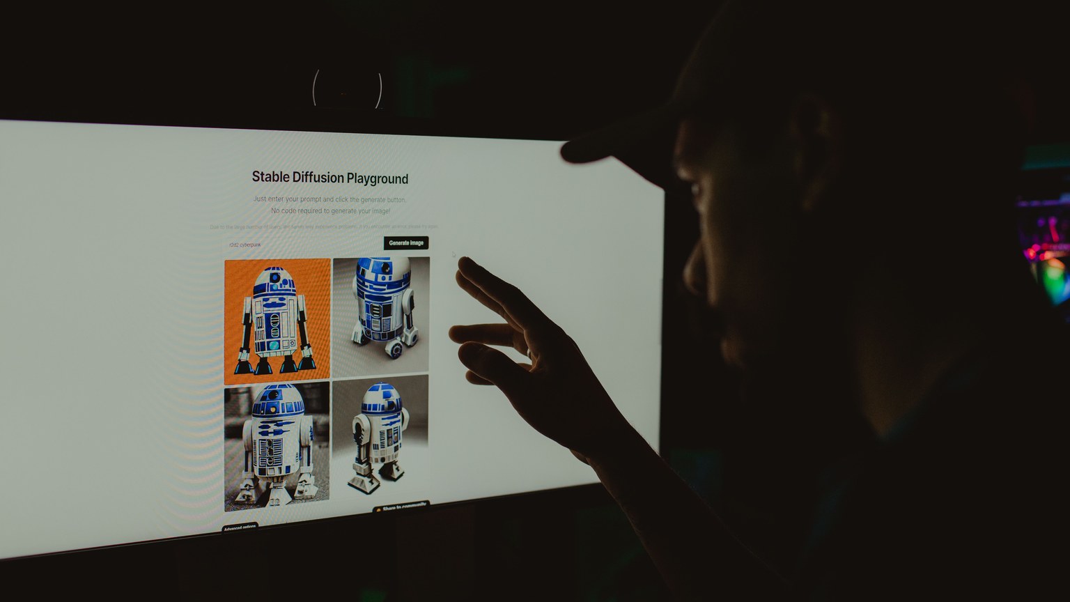 Person interacts with robot images on a screen in a dark room, highlighting technology use.