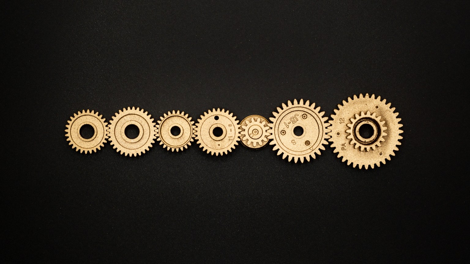 An artistic arrangement of golden gears on a dark backdrop, symbolizing mechanics and cooperation.