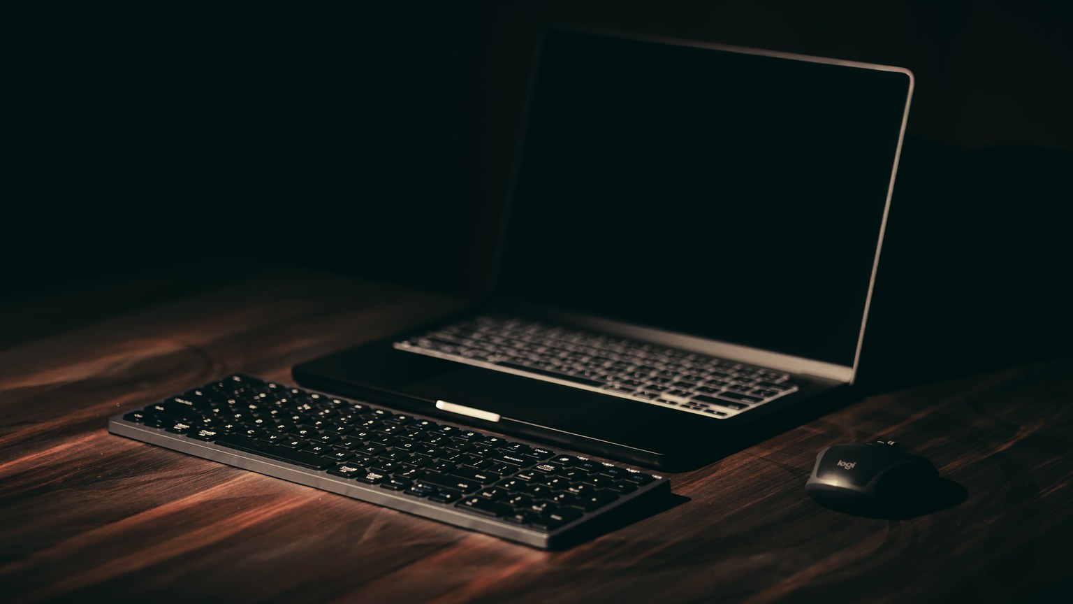 Minimalist dark-themed workspace with laptop and wireless keyboard.