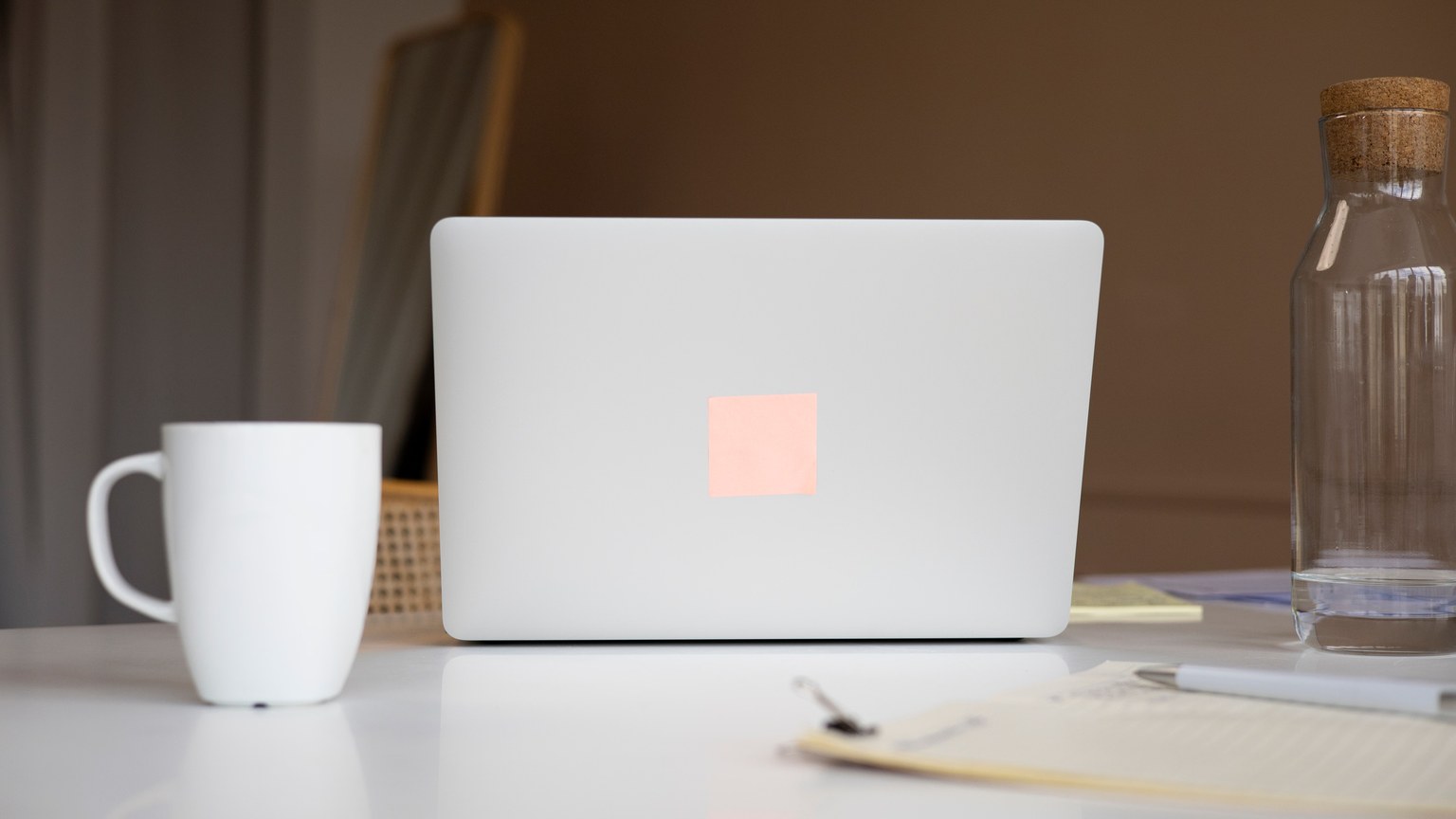 Modern minimalist workspace with a laptop, ceramic mug, and glass water bottle on a white surface.