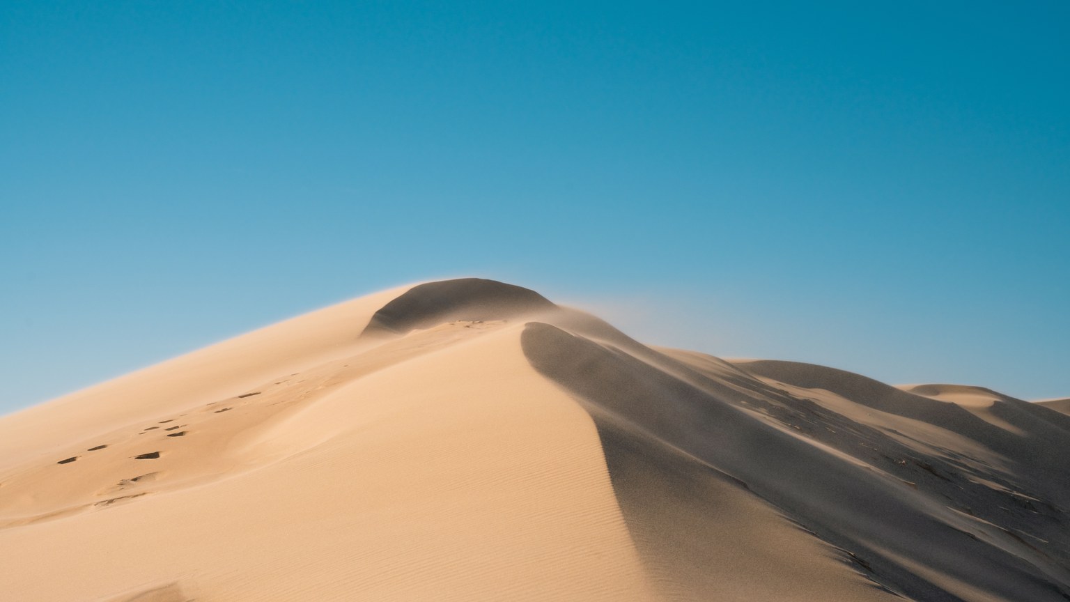 Wide-angle view of a towering sand dune against a vibrant blue sky, showcasing the beauty of desert landscapes.