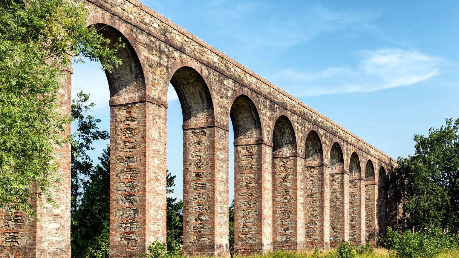 Scenic view of an ancient Roman aqueduct in Tuscany, showcasing historic architecture.